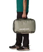 Side of man carrying a Patagonia 30 litre black hole travel backpack in beige over the shoulder using the carry handle 