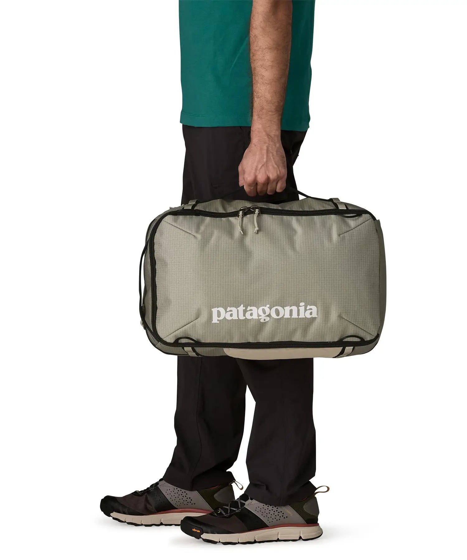 Side of man carrying a Patagonia 30 litre black hole travel backpack in beige over the shoulder using the carry handle 