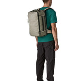 Man carrying a Patagonia 30 litre black hole travel backpack in beige using the shoulder and hip straps