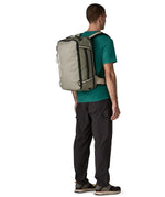 Man carrying a Patagonia 30 litre black hole travel backpack in beige using the shoulder and hip straps
