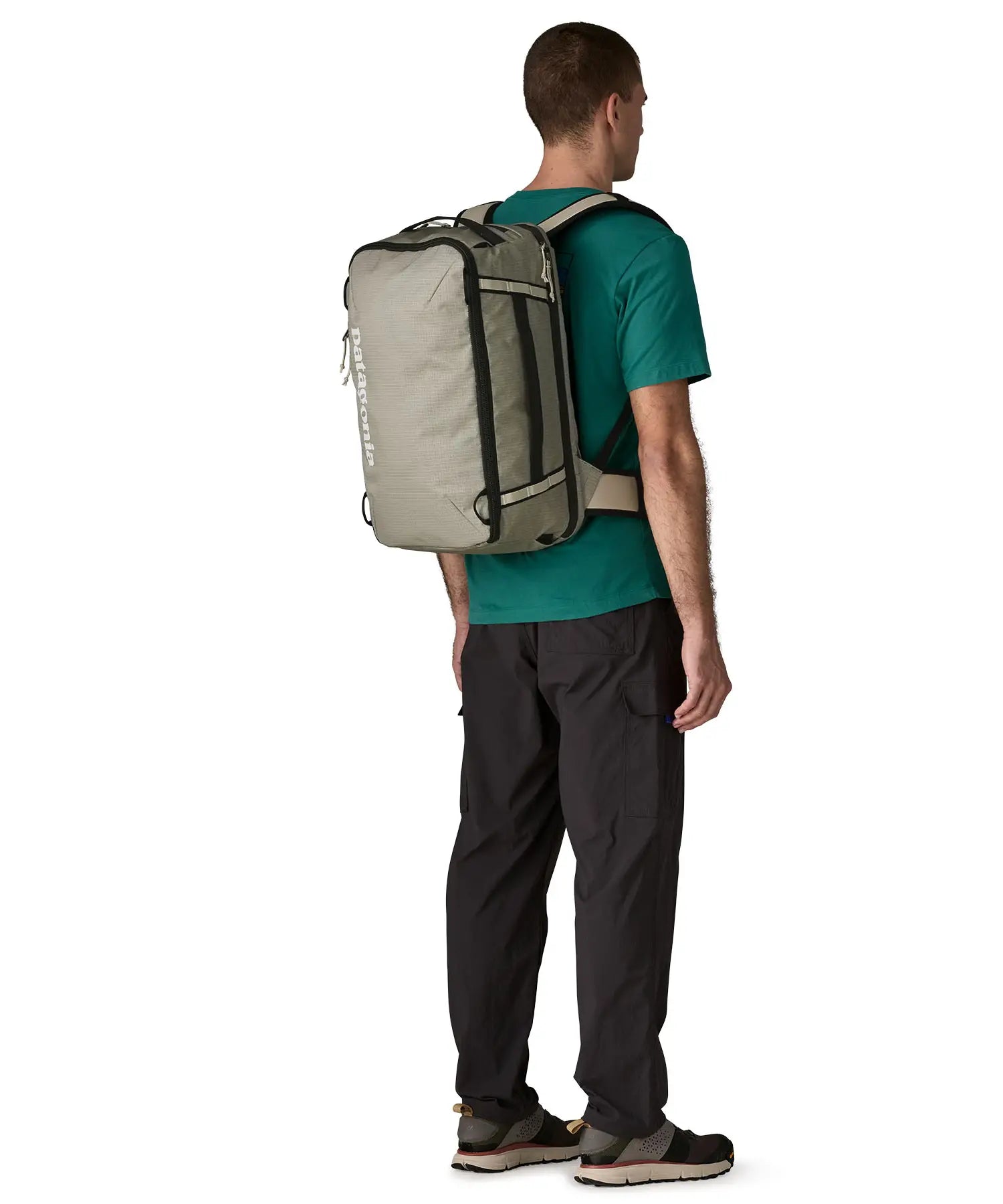 Man carrying a Patagonia 30 litre black hole travel backpack in beige using the shoulder and hip straps