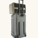 Patagonia 30 litre black hole weather resistant travel backpack in beige on top of a wheeled duffel bag through a loop on the back