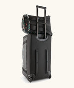 Patagonia black hole backpack 25L in black with repeating abstract pattern design resting on large wheeled duffel bag