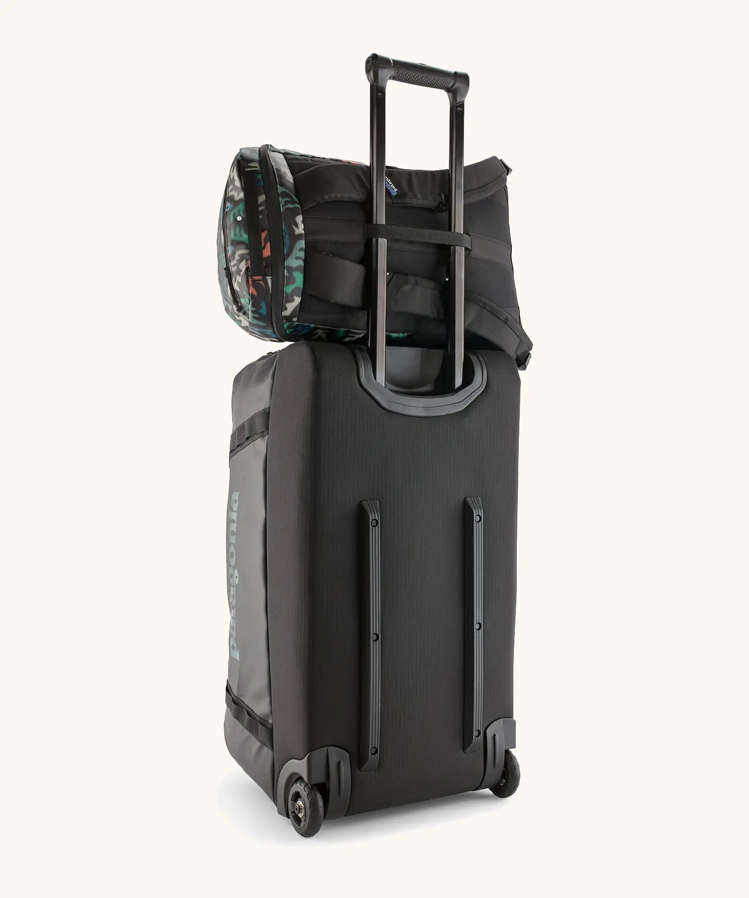 Patagonia black hole backpack 25L in black with repeating abstract pattern design resting on large wheeled duffel bag