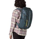 Woman carrying a Patagonia 100% recycled polyester black hole 25 litre backpack in teal on the back 