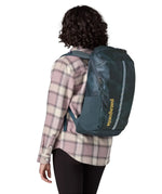 Woman carrying a Patagonia 100% recycled polyester black hole 25 litre backpack in teal on the back 
