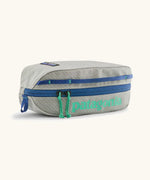 Patagonia 3L black hole cube travel bag in light grey and blue trim. Showing a zip fastener with the brand name on the top panel