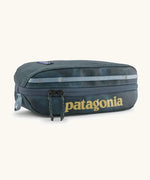 Patagonia 3L black hole cube travel bag in teal and light blue trim. Showing a zip fastener with the brand name on the top panel