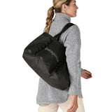 Woman carrying a Patagonia weather resistant packable black hole 25 litre tote bag in black over the shoulder using the long carry handles