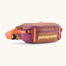 Patagonia black hole waist 5L pack in pale orange with 2 compartments and purple mesh side pockets and clip buckle fastener 