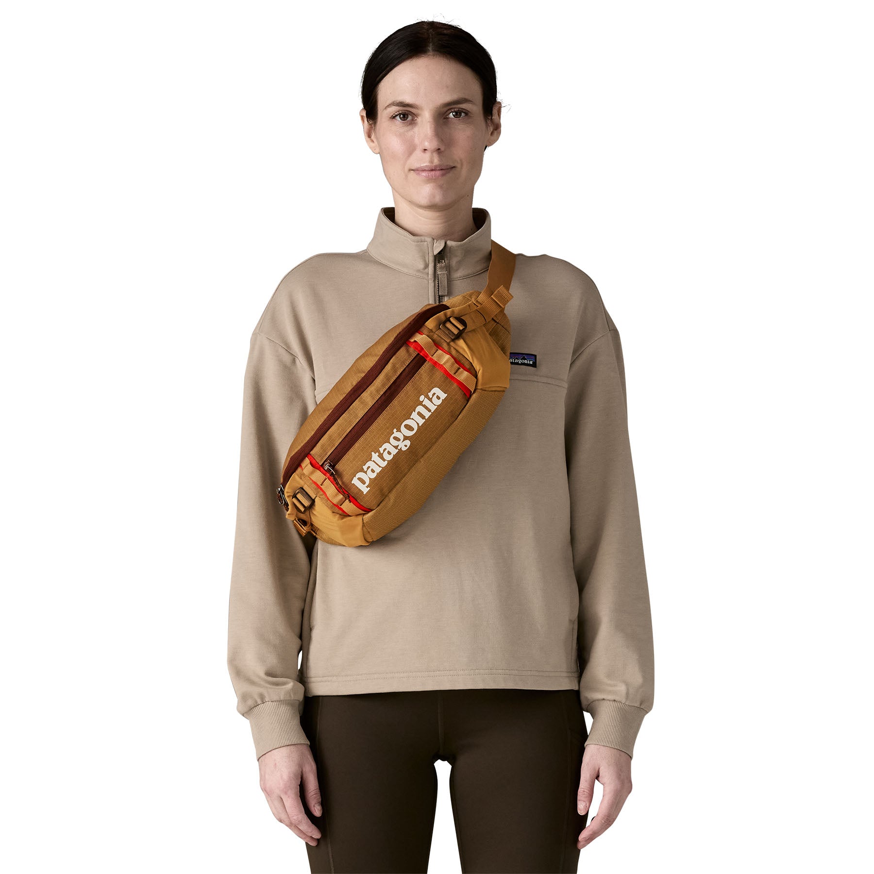 A woman wearing the patagonia waist pack over the shoulder in talon gold available at Babipur.. A 100% recycled material pack with 2 main compartments and adjustable shoulder strap.