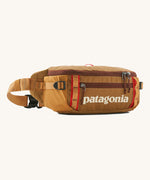 Patagonia black hole waist 5L pack in talon gold. A 100% recycled nylon pack in dark yellow with dark red detail. Features 2 compartments with mesh side pockets and a buckle fastener 