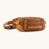Patagonia 100% recycled nylon black hole waist 5L pack in cinnamon brown showing 2 compartments with mesh side pockets and buckle fastener 