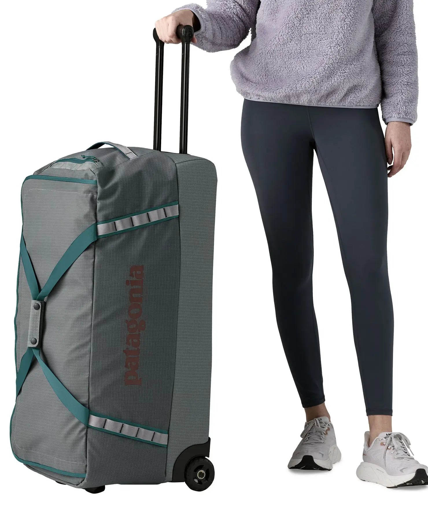 Woman holding the pull handle on the Patagonia's black hole wheeled 100L duffel bag in dark grey.