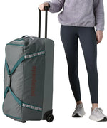 Woman holding the pull handle on the Patagonia's black hole wheeled 100L duffel bag in dark grey.