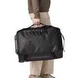 Woman pulling a Patagonia 40 litres black hole wheeled duffel bag in all black using the carry handle on the side