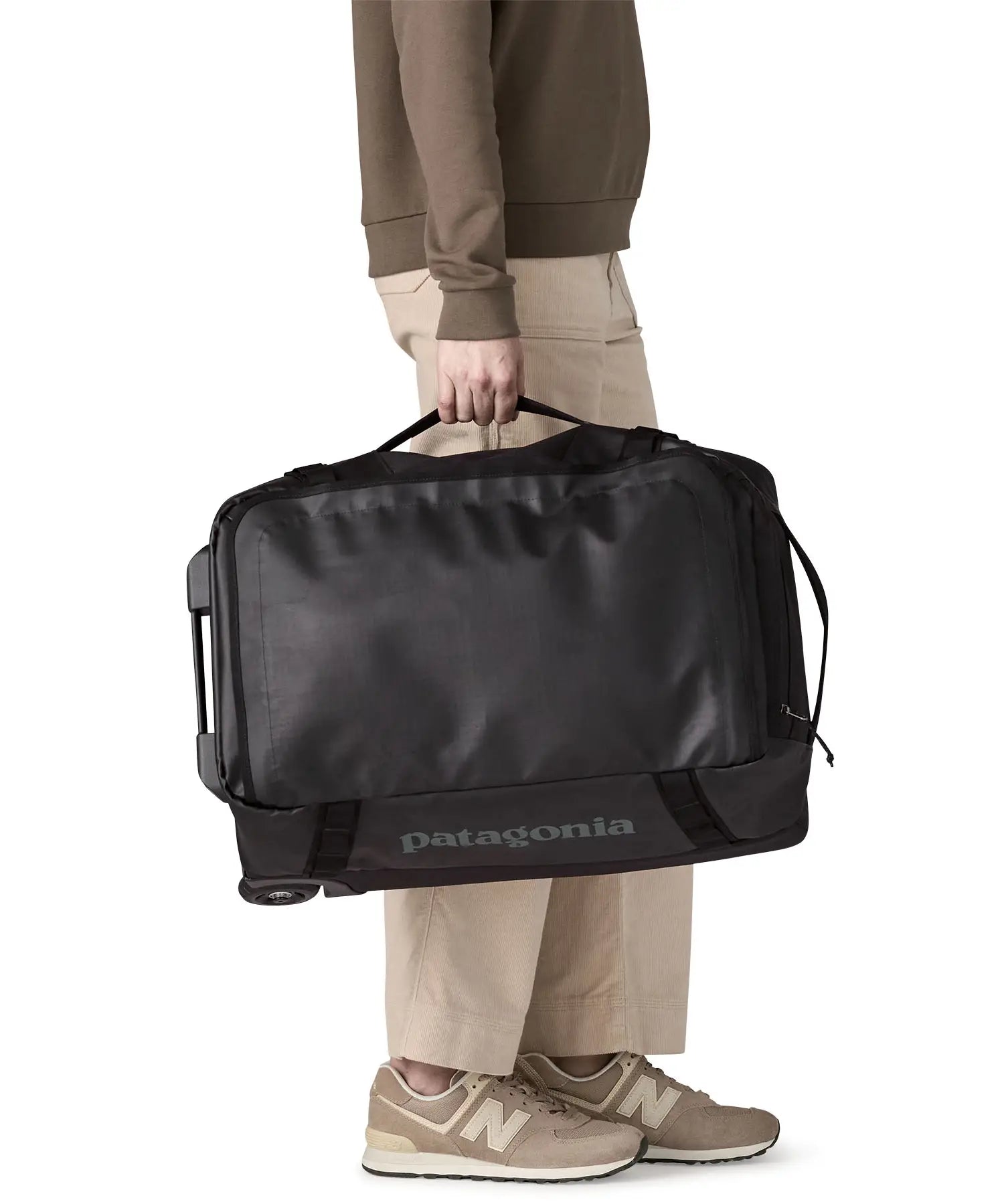 Woman pulling a Patagonia 40 litres black hole wheeled duffel bag in all black using the carry handle on the side