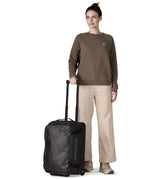 Woman holding the retractable handle on the Patagonia 40 litres black hole wheeled duffel bag in all black 