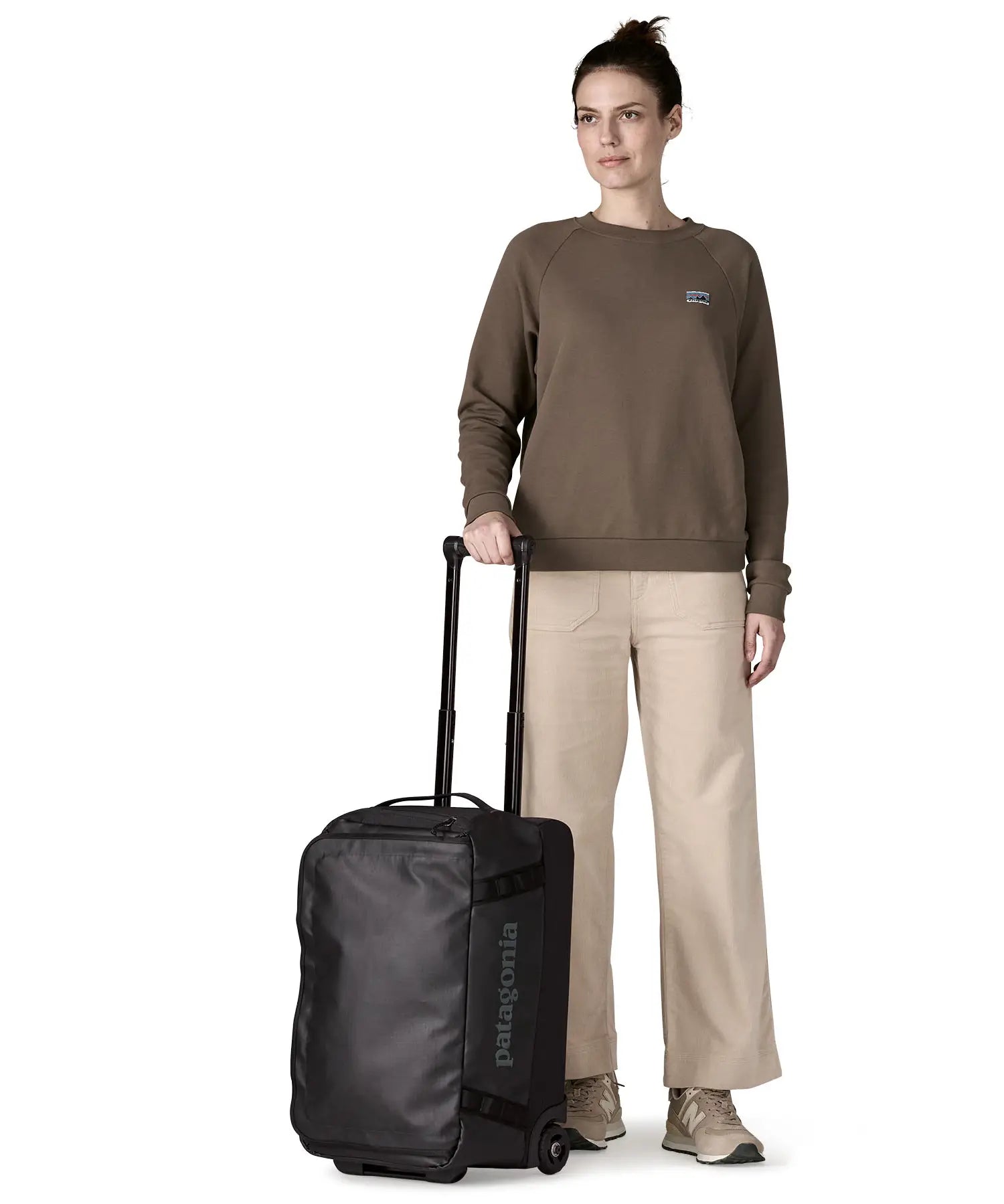 Woman holding the retractable handle on the Patagonia 40 litres black hole wheeled duffel bag in all black 