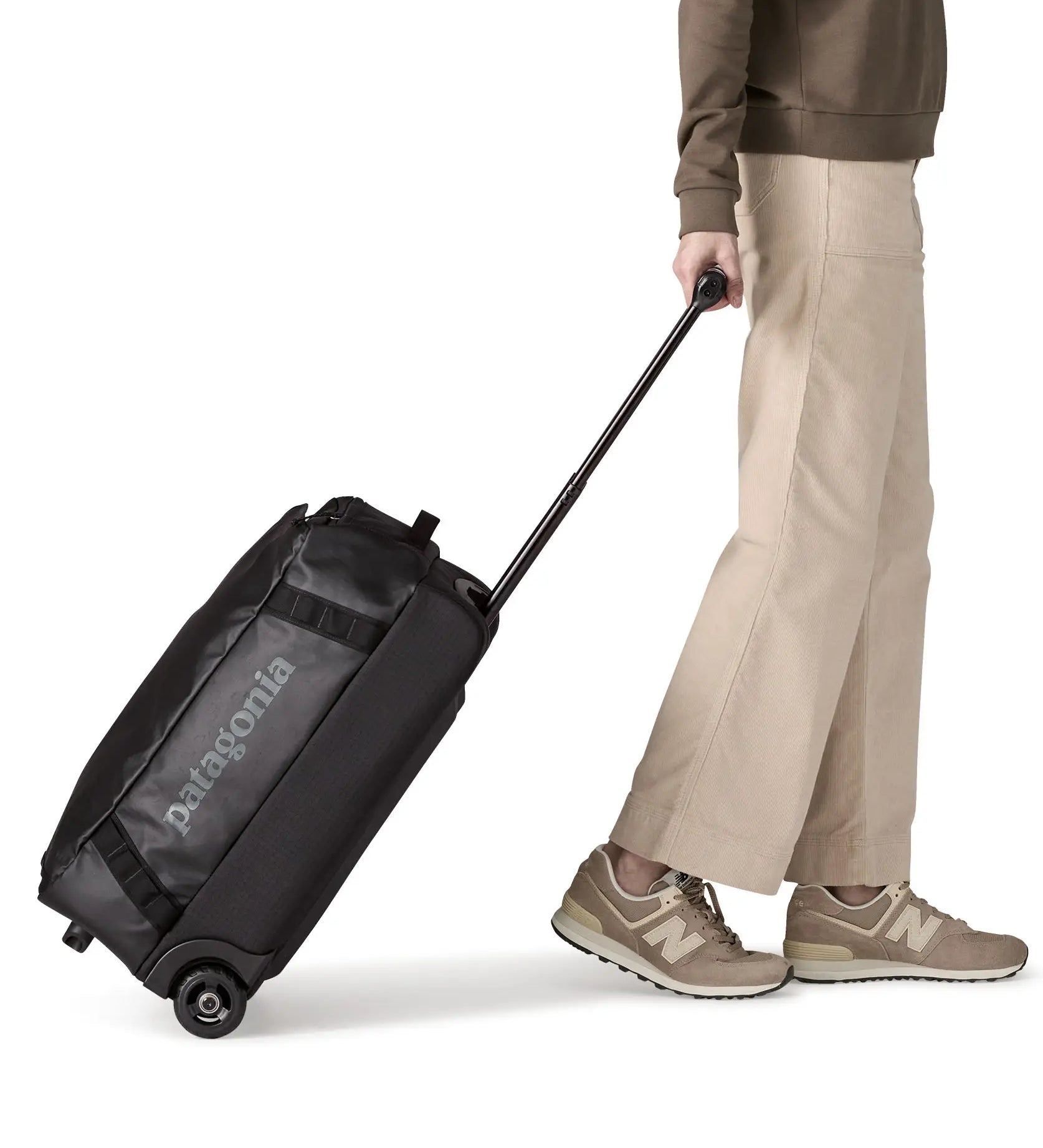 Woman pulling a Patagonia 40 litres black hole wheeled duffel bag in all black using the retractable handle