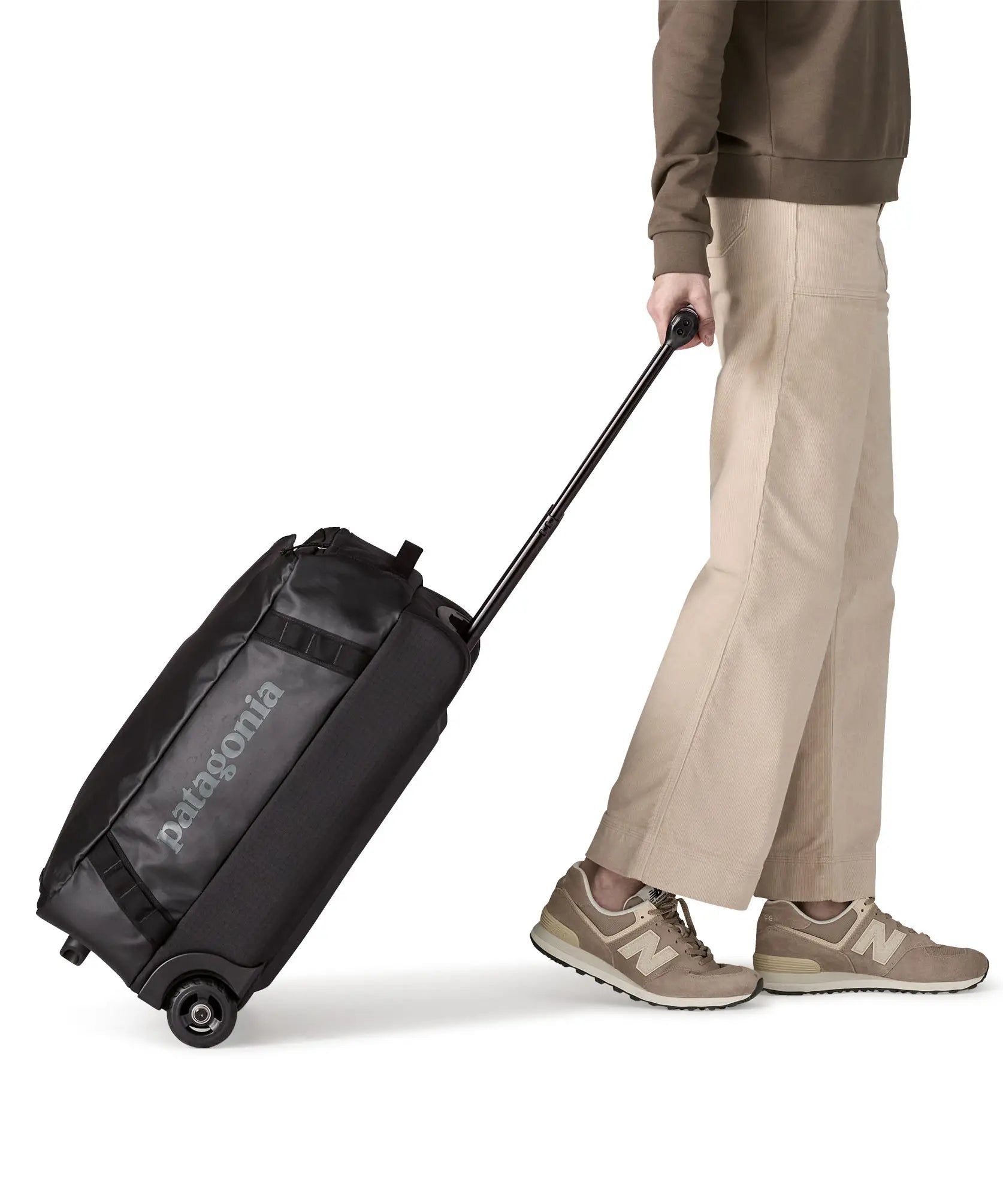 Woman pulling a Patagonia 40 litres black hole wheeled duffel bag in all black using the retractable handle