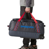 Man carrying a Patagonia dark blue hole wheeled large capacity 70L duffel bag by the red carry straps showing brand name on the side