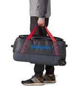 Man carrying a Patagonia dark blue hole wheeled large capacity 70L duffel bag by the red carry straps showing brand name on the side