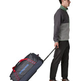 Man pulling along a Patagonia dark blue hole wheeled large capacity 70L duffel bag by the retractable handle.