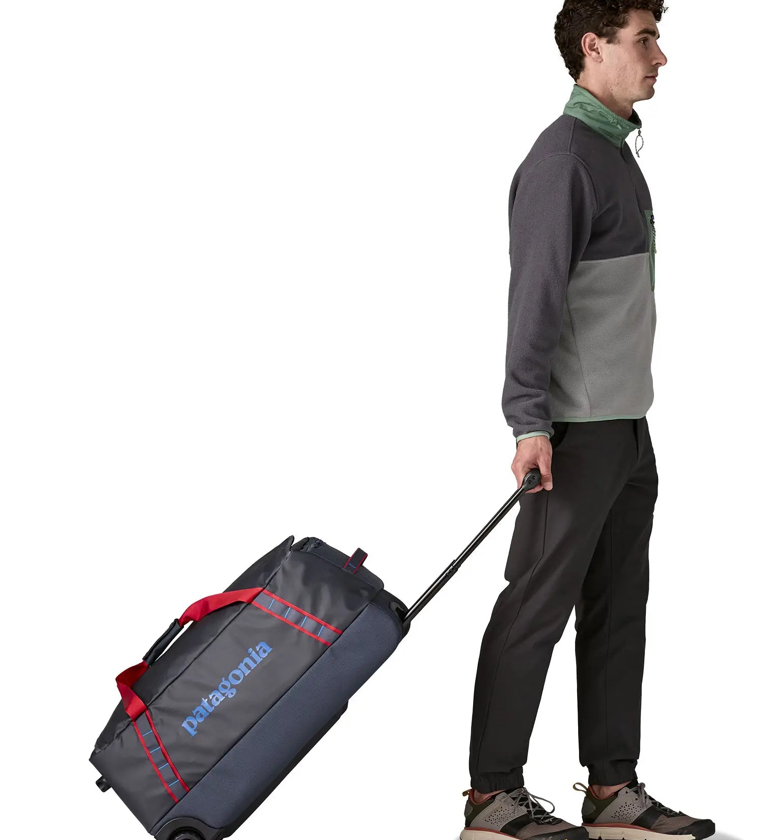 Man pulling along a Patagonia dark blue hole wheeled large capacity 70L duffel bag by the retractable handle.