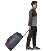 Man pulling along a Patagonia dark blue hole wheeled large capacity 70L duffel bag by the retractable handle.