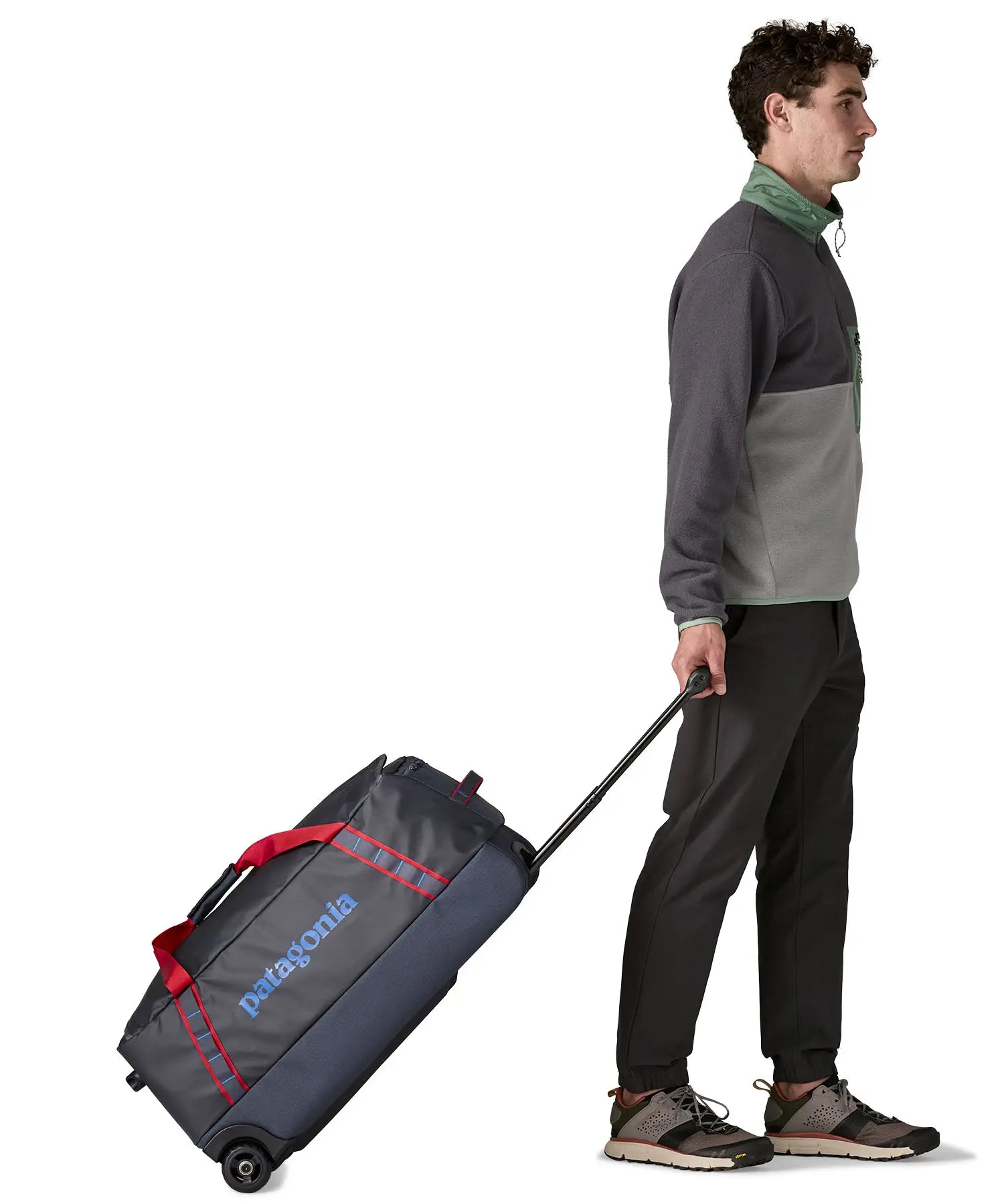 Man pulling along a Patagonia dark blue hole wheeled large capacity 70L duffel bag by the retractable handle.