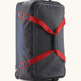 Patagonia black hole 70 litre wheeled duffel bag in dark blue with red straps. Features extra loops for attaching small items and retractable handle
