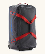 Patagonia black hole 70 litre wheeled duffel bag in dark blue with red straps. Features extra loops for attaching small items and retractable handle