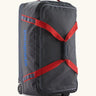 Patagonia black hole 70 litre wheeled duffel bag in dark blue with red straps. Features extra loops for attaching small items and retractable handle