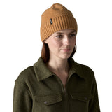 A woman wearing the Patagonia adult brodeo beanie hat in talon gold available at Babipur. A soft knit style beanie with turn up brim and logo patch on the side