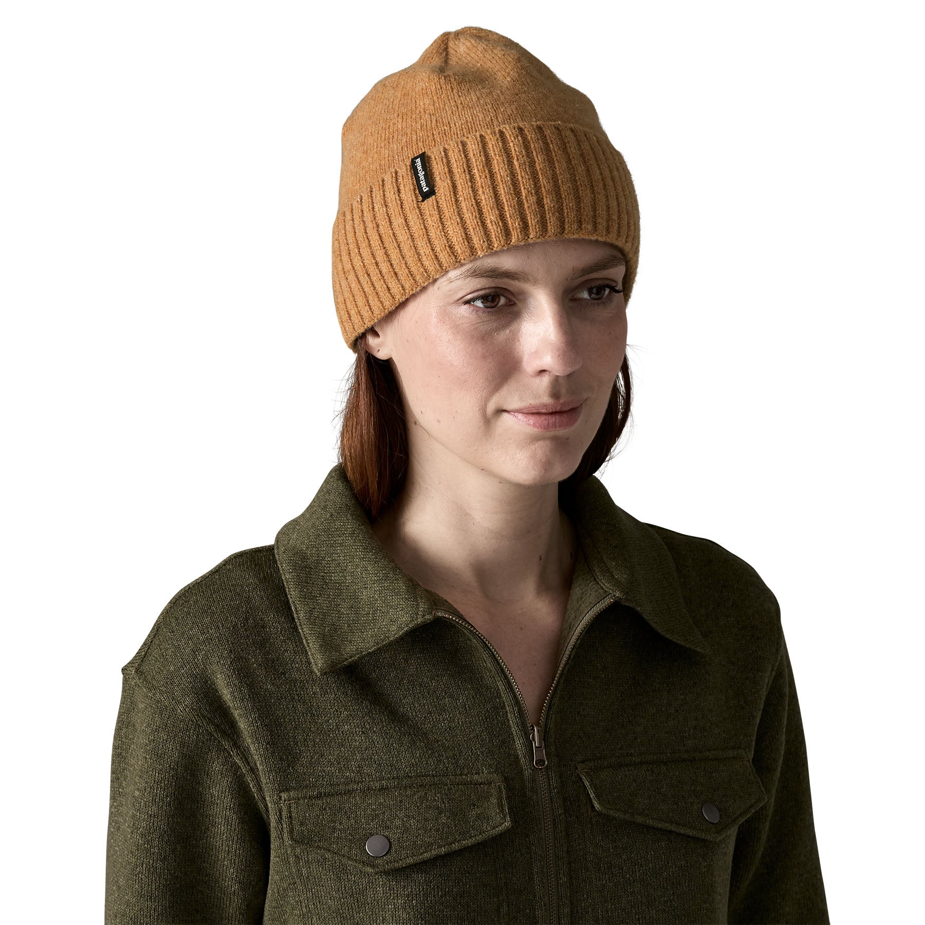 A woman wearing the Patagonia adult brodeo beanie hat in talon gold available at Babipur. A soft knit style beanie with turn up brim and logo patch on the side