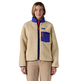 A woman wearing the Patagonia women's classic retro-x jacket in a dark natural colour way available at Babipur. A thick fleece with royal blue trim detail with a full length zip, 2 side pockets and a chest pocket with the logo patch stitched above.