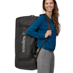 A person carrying the Patagonia Black Hole Duffel 100L Black on their back with the shoulder straps