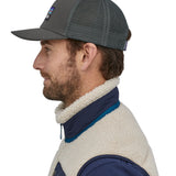 A person wearing the Patagonia P-6 Logo Trucker Hat - Forge Grey, showing it from the side to show the mesh at the back