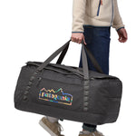 A person carrying the Patagonia Black Hole Duffel 100L Ink Black in their hand using the handle straps