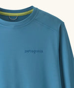 Close up of Patagonia kids long sleeve capilene tshirt in bright blue showing brand name on chest and light green trim on inner collar