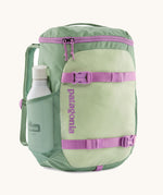Patagonia refugito 18 litres daypack in ellwood green. A pastel green backpack with 2 side mesh pockets, pink buckle, fasteners on the front to keep it secure and a zip on the top for easy access with padded shoulder straps.