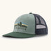 Patagonia Kids Trucker hat in Cover Green. Organic sage green front crown with retro style Patagonia Fitz Roy Foothills logo, Forest green brim, and grey recycled polyester mesh back. 