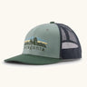 Patagonia Kids Trucker hat in Cover Green. Organic sage green front crown with retro style Patagonia Fitz Roy Foothills logo, Forest green brim, and grey recycled polyester mesh back. 