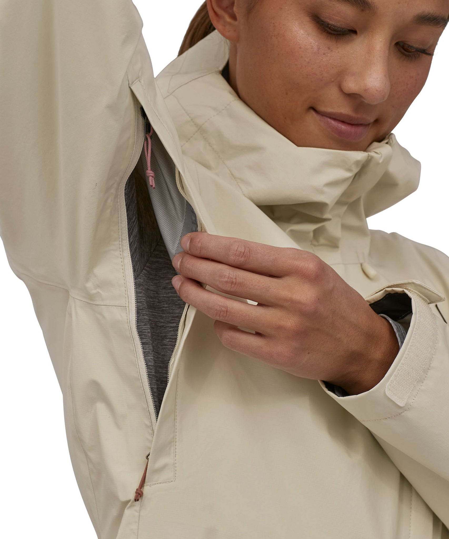 A zipped area under the arms of the Patagonia Women's Torrentshell 3L Rain Jacket, to show the jacket is breathable. A person is wearing the jacket and is showing the fabric area inside the coat under the arms