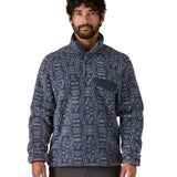 A man wearing the Patagonia mens synchilla jacket available at Babipur. A lightweight fleece in dark blue colour with a white flowing pattern all over. Features a chest pocket, logo patch stitched above and a 1/4 length popper fastener.