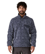 A man wearing the Patagonia mens synchilla jacket available at Babipur. A lightweight fleece in dark blue colour with a white flowing pattern all over. Features a chest pocket, logo patch stitched above and a 1/4 length popper fastener.