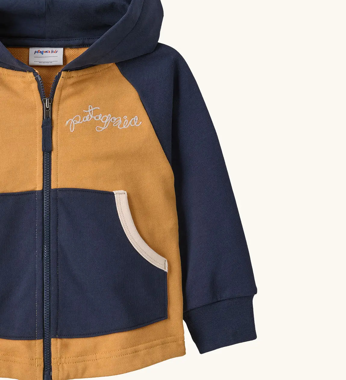 Patagonia 100% organic cotton little kids full zip hoody in warm mango showing close up of embroidered brand logo on the chest and pouch pocket