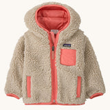 Patagonia little kids retro x hoody in dark natural available at Babipur. A 100% recycled polyester thick pile fleece hooded jacket in cream with pink trim Features a full length zip, 2 side pockets and a small chest pocket