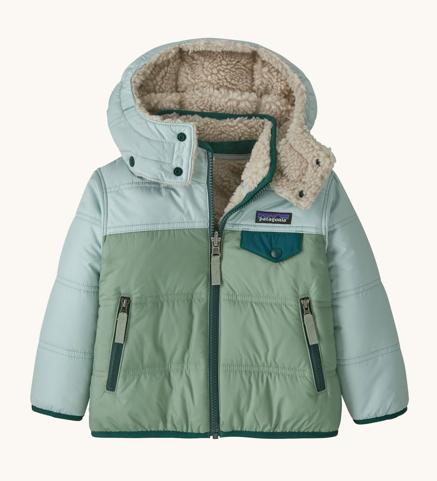 Patagonia little kids tribbles hoody available at Babipur. A reversible coat showing a green and blue hooded coat and natural fleece inner for warmth. Features a small chest pocket with popper fastening and 2 side zip pockets